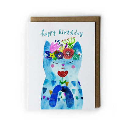 A soft white birthday card with the words Happy Birthday in blue on the top of the card. The front has a colorful painting of a blue kitty adorned with colorful flowers. 